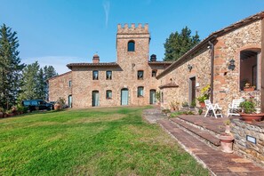 A stone building with a tower, a grassy yard, and outdoor seating. - Rosmarinus Apartment – Two-Room Flat with Views of Tuscan Vineyards (San Casciano In Val di Pesa)