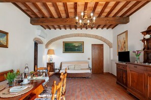 A room with a bed, a dining table with chairs, a TV, and a chandelier. - Rosmarinus Apartment – Two-Room Flat with Views of Tuscan Vineyards (San Casciano In Val di Pesa)