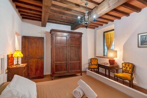 A room with a bed, a wooden wardrobe, a table with chairs, a chandelier, and a window with curtains. - Rosmarinus Apartment – Two-Room Flat with Views of Tuscan Vineyards (San Casciano In Val di Pesa)