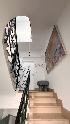 A staircase with a black metal railing, a light fixture above, a door at the top, and a painting on the wall. - "La Grande Terrasse" Apartment with 40m2 Private Terrace, Wi-Fi, and Air Conditioning (Cannes)