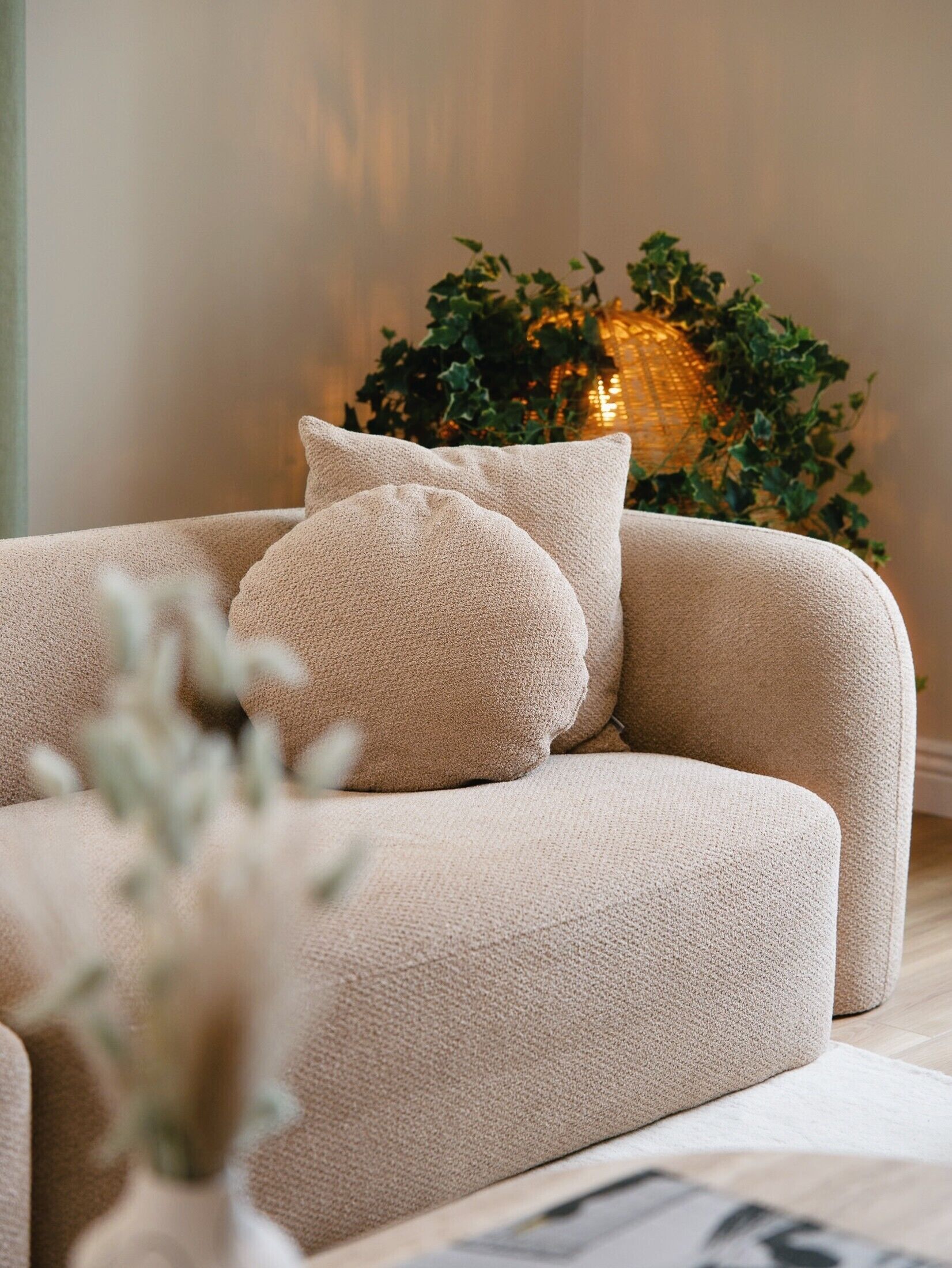 Un canapé beige avec deux coussins, une plante en pot et un mur à texture en arrière-plan.