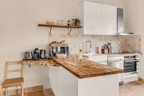 A modern kitchen with a wooden countertop, white cabinets, a built-in oven, and a coffee machine. - "La Grande Terrasse" Apartment with 40m2 Private Terrace, Wi-Fi, and Air Conditioning (Cannes)