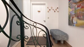 A staircase with a metal railing, a white door, a wall-mounted art piece, and a textured bench. - "La Grande Terrasse" Apartment with 40m2 Private Terrace, Wi-Fi, and Air Conditioning (Cannes)