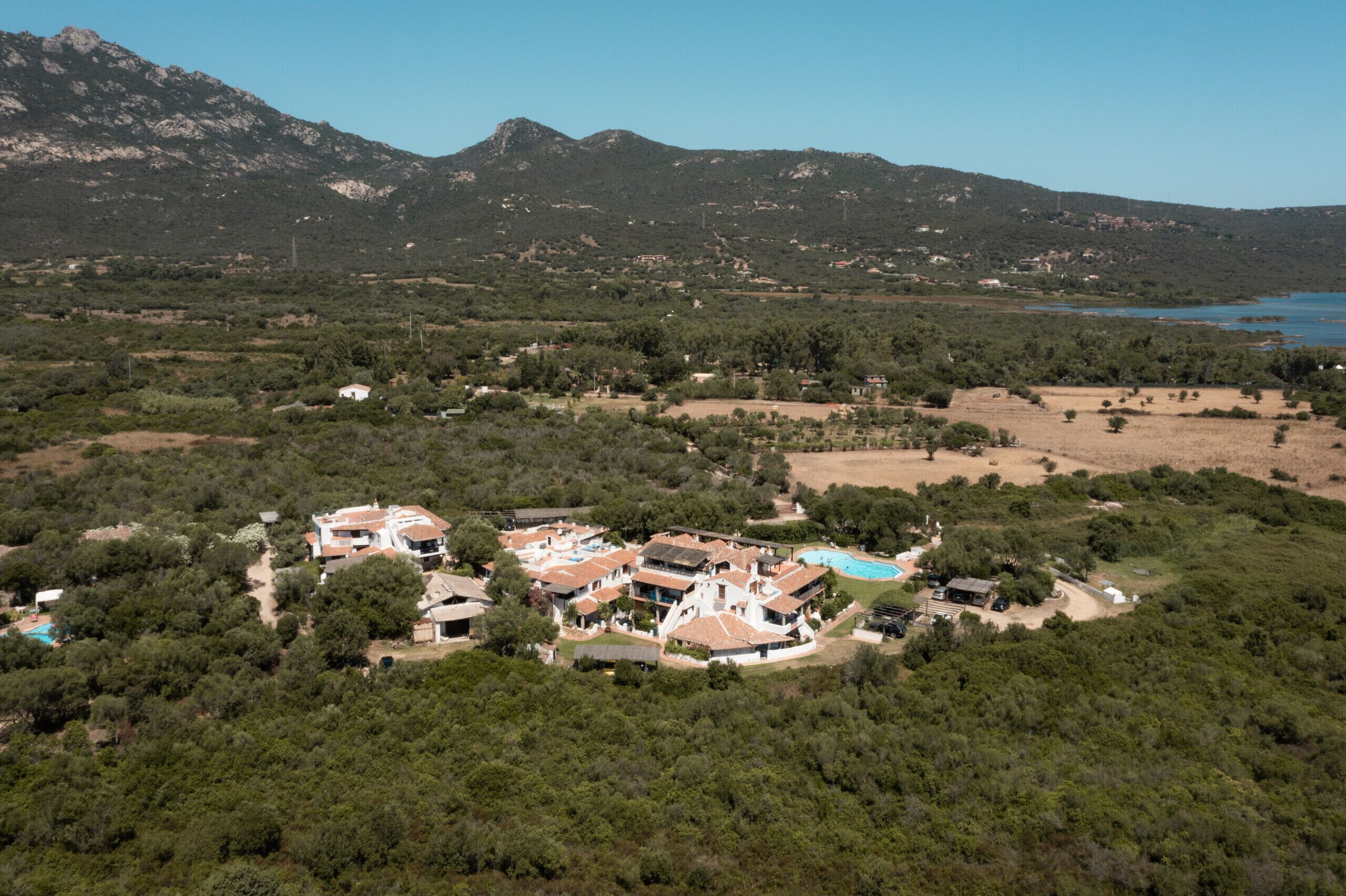 A coastal property with multiple buildings, a swimming pool, and a view of the sea and mountains.