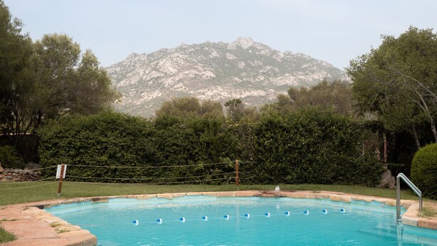 Una piscina con agua azul cristalina, rodeada de vegetación y una montaña al fondo.