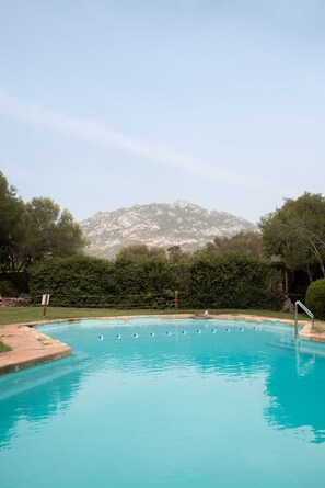 Une piscine à l’eau d’un bleu cristallin, entourée de verdure, avec une montagne en toile de fond.