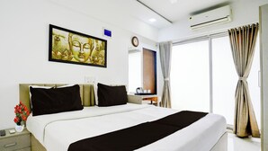 A hotel room with a large bed, a nightstand, a bedside table, a wall-mounted clock, and a window with curtains. - Collection O Jupiter Hospital Thane West (Mumbai)
