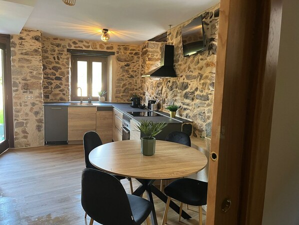 Una cocina con paredes de piedra, una mesa de madera y sillas negras.