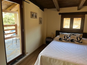 A bedroom with a bed, two pillows, a nightstand, a window, and a door leading to an outdoor area.