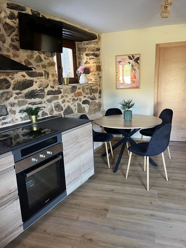 A kitchen with a stone wall, a built-in oven, and a dining area with a round table and chairs.