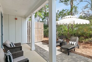 Une terrasse extérieure avec des meubles en osier, un parasol blanc et une clôture en bois.