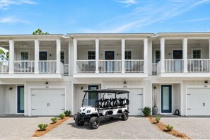 Un immeuble résidentiel à plusieurs étages, doté d’un espace de stationnement couvert, de portes de garage numérotées et d’une voiturette de golf garée devant.