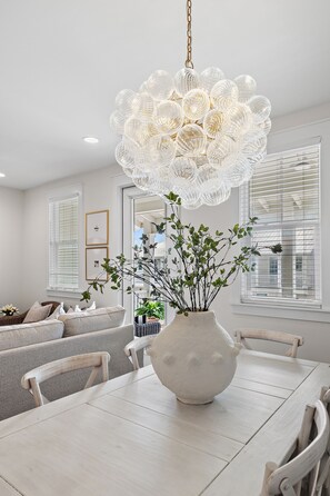 A dining area with a white table, chairs, a white vase with branches, and a chandelier. - Welcome Home to 30A – FREE Golf Cart (Santa Rosa Beach)