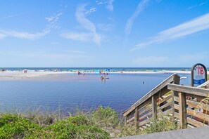 Une plage avec une promenade en bois menant à l’eau, un ciel dégagé et un panneau indiquant l’accès à la plage.