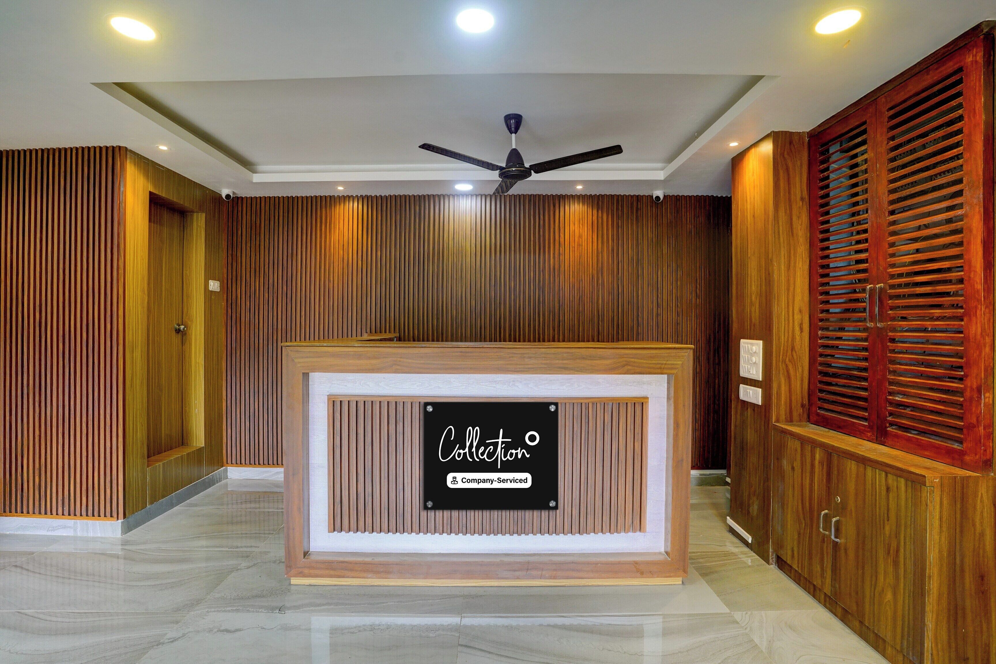 A reception desk with a sign indicating it's company-serviced, wooden paneling on the walls, a ceiling fan, and a polished marble floor.