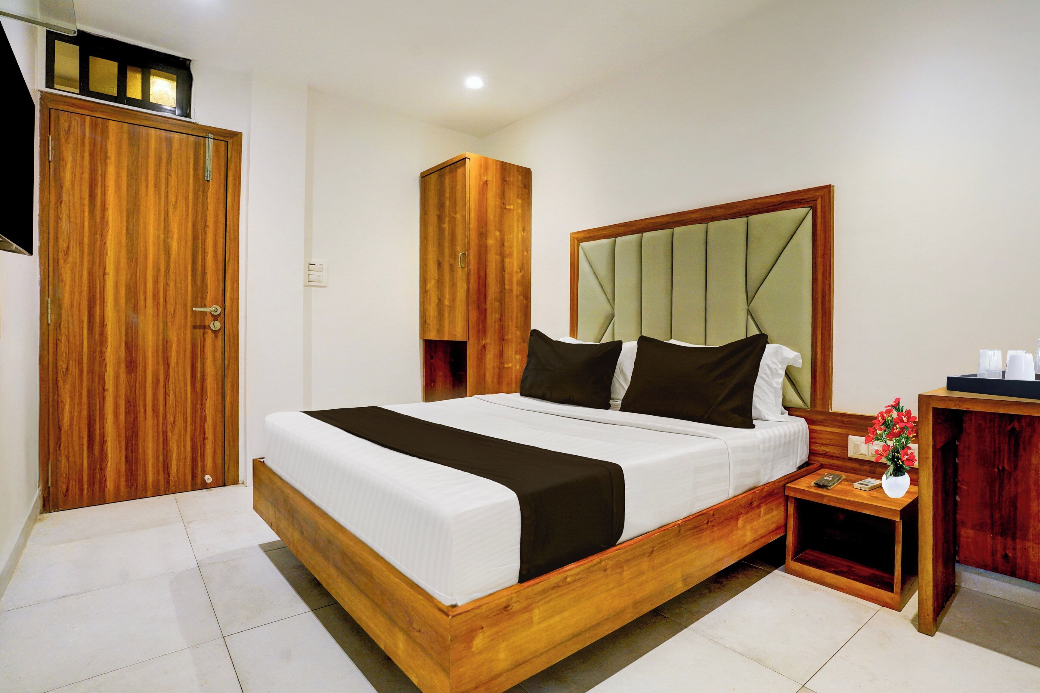 A hotel room with a wooden bed, a wardrobe, a bedside table with a vase of flowers, and a nightstand.