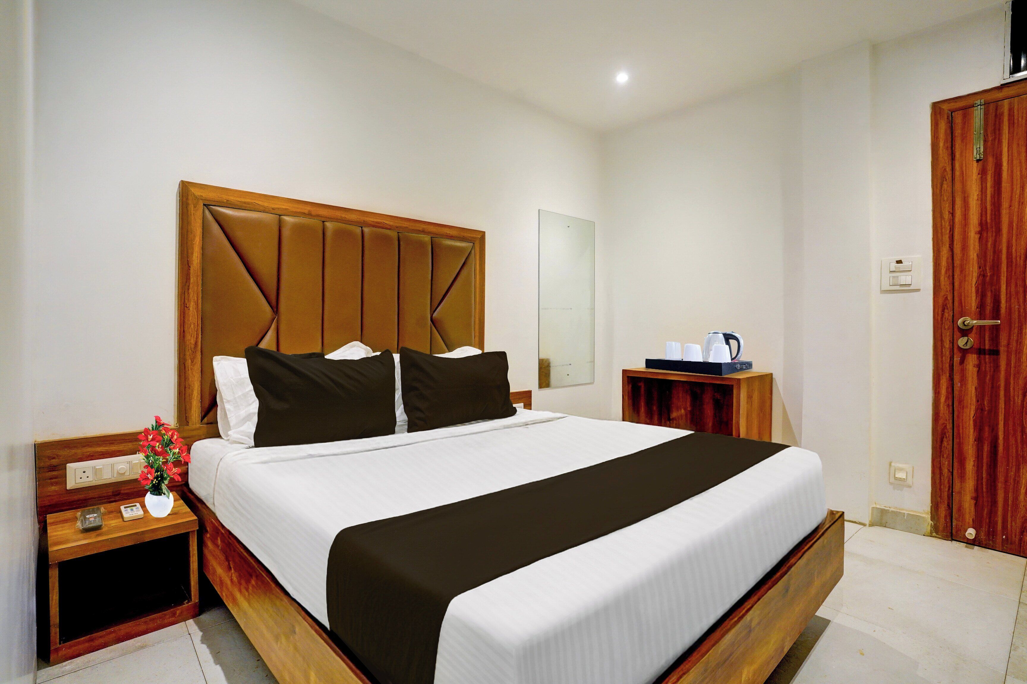 Habitación de hotel con una cama grande, cabecera de madera, mesitas de noche, un velador, un espejo, un armario y un pequeño escritorio con una lámpara.