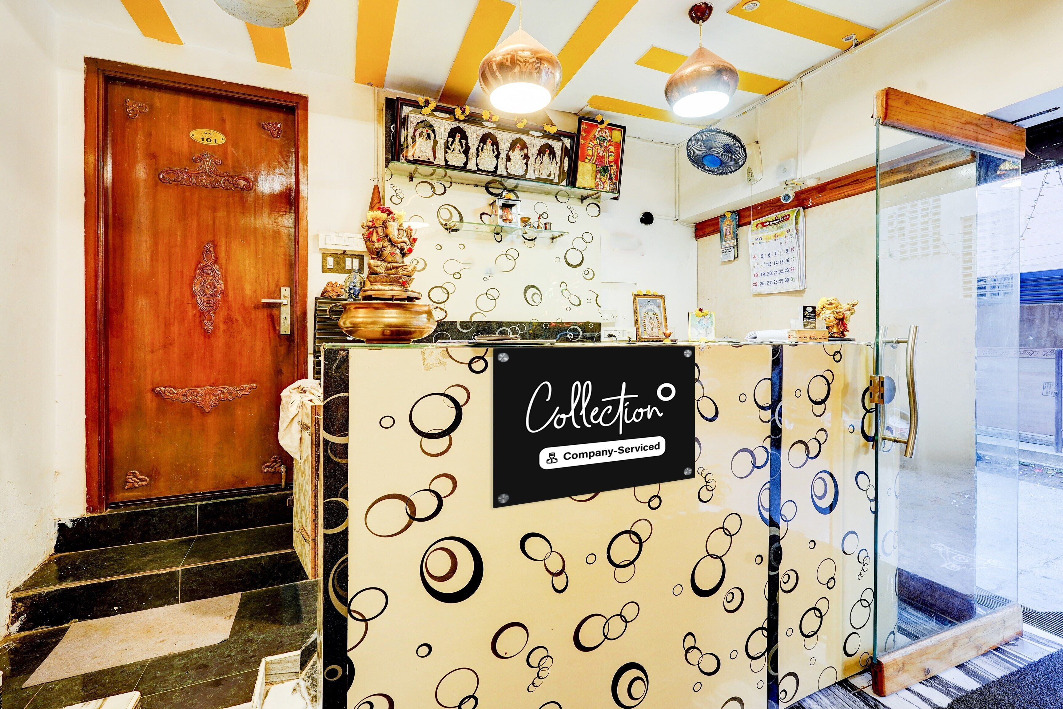 Un área de recepción con una puerta de madera, un mostrador de recepción con un letrero que dice 'Collection' y un calendario en la pared.