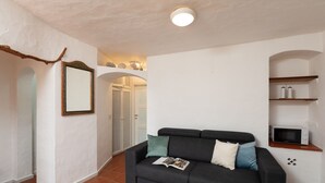 Un salon avec un canapé noir, une petite table, un miroir fixé au mur et un four à micro-ondes posé sur une étagère.