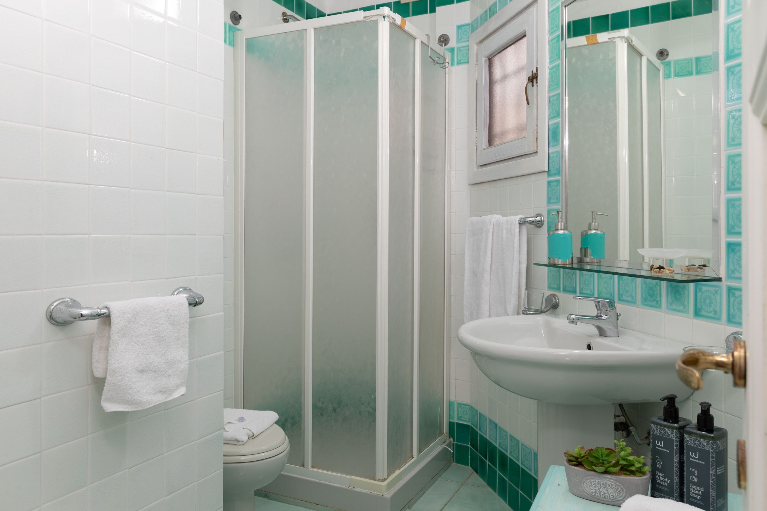 Une salle de bain avec des toilettes blanches, une douche en verre, un lavabo avec un miroir et des articles de toilette posés sur le comptoir.