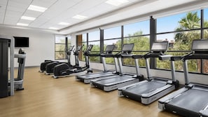 Ein Fitnessraum mit mehreren Laufbändern, einem Ergometer und einem Fernsehbildschirm.
