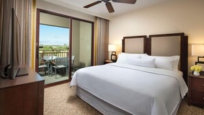 Habitación de hotel con una cama grande, un escritorio, una silla, un balcón con mesa y sillas, y un ventilador de techo.