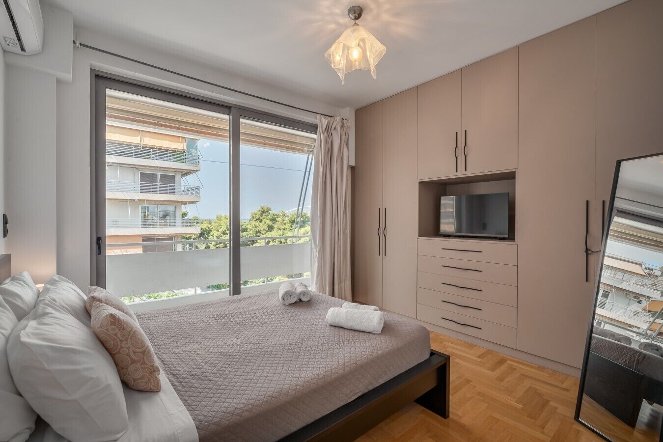 A bedroom with a bed, a TV, and a sliding glass door to a balcony.