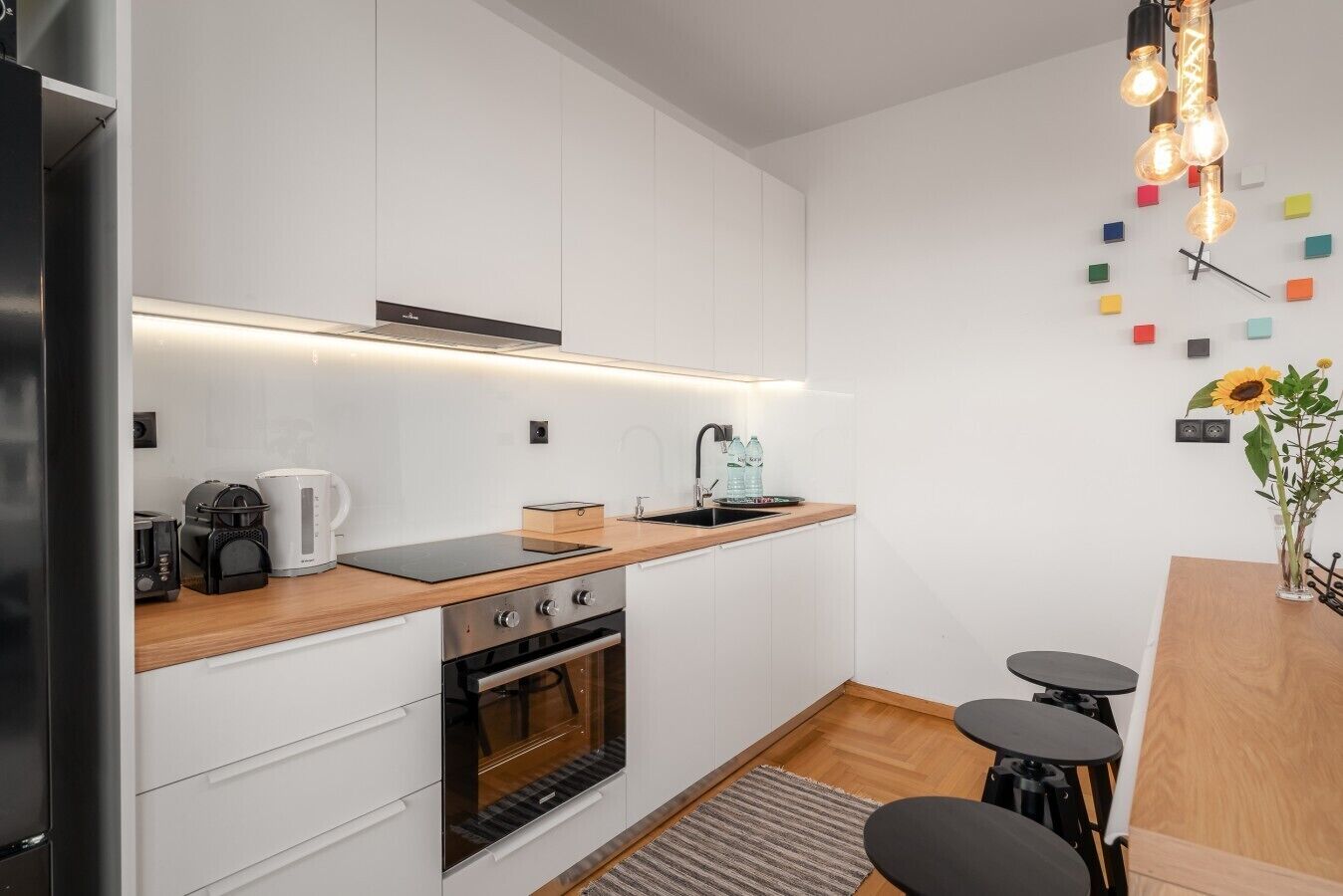 Une cuisine moderne avec des meubles blancs, un plan de travail en bois, un four encastré et une machine à café.