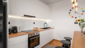 A modern kitchen with white cabinets, a wooden countertop, a built-in oven, and a coffee maker.