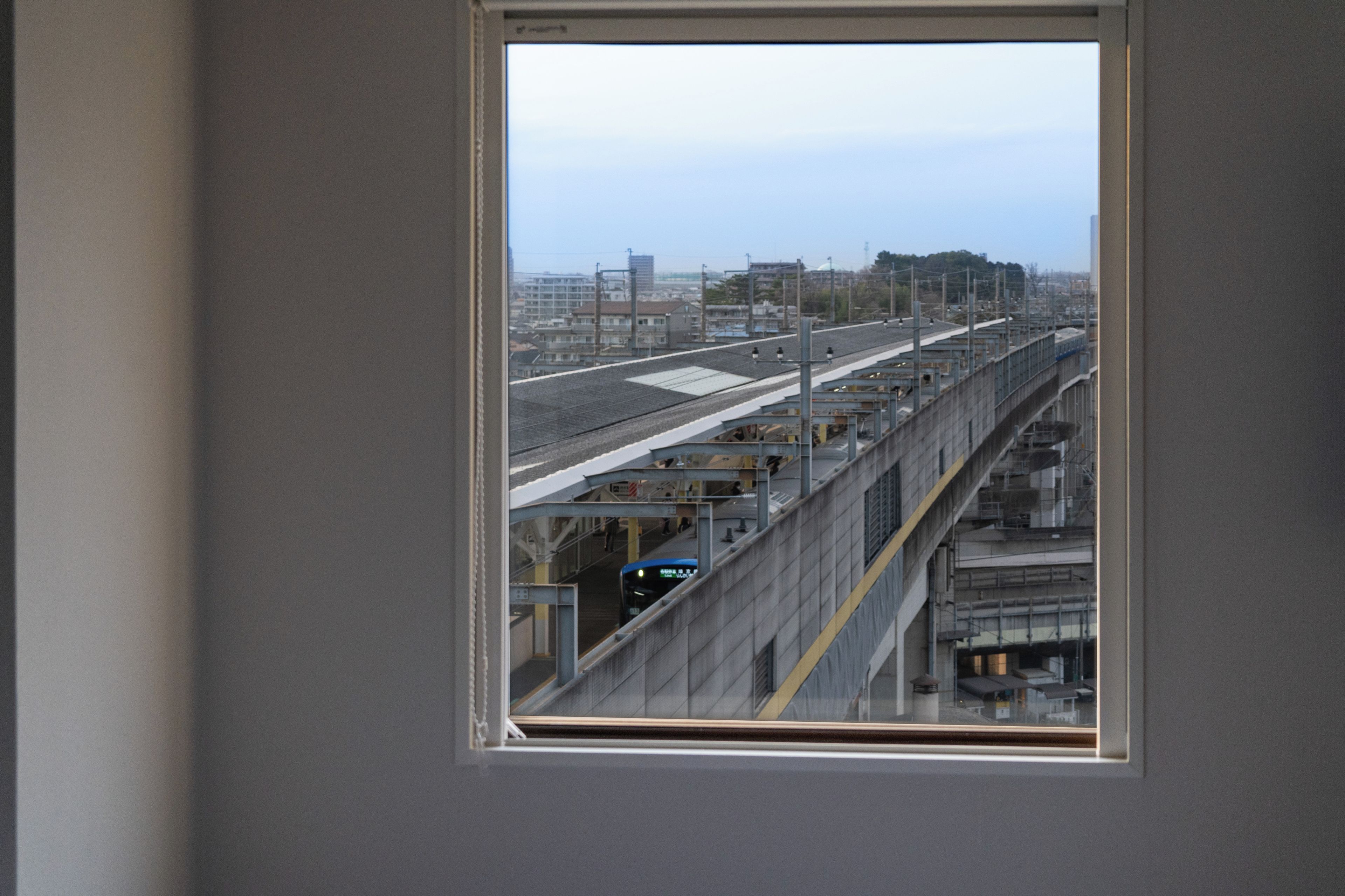 Vista desde una ventana de un andén de estación de tren, con vías y un tren.