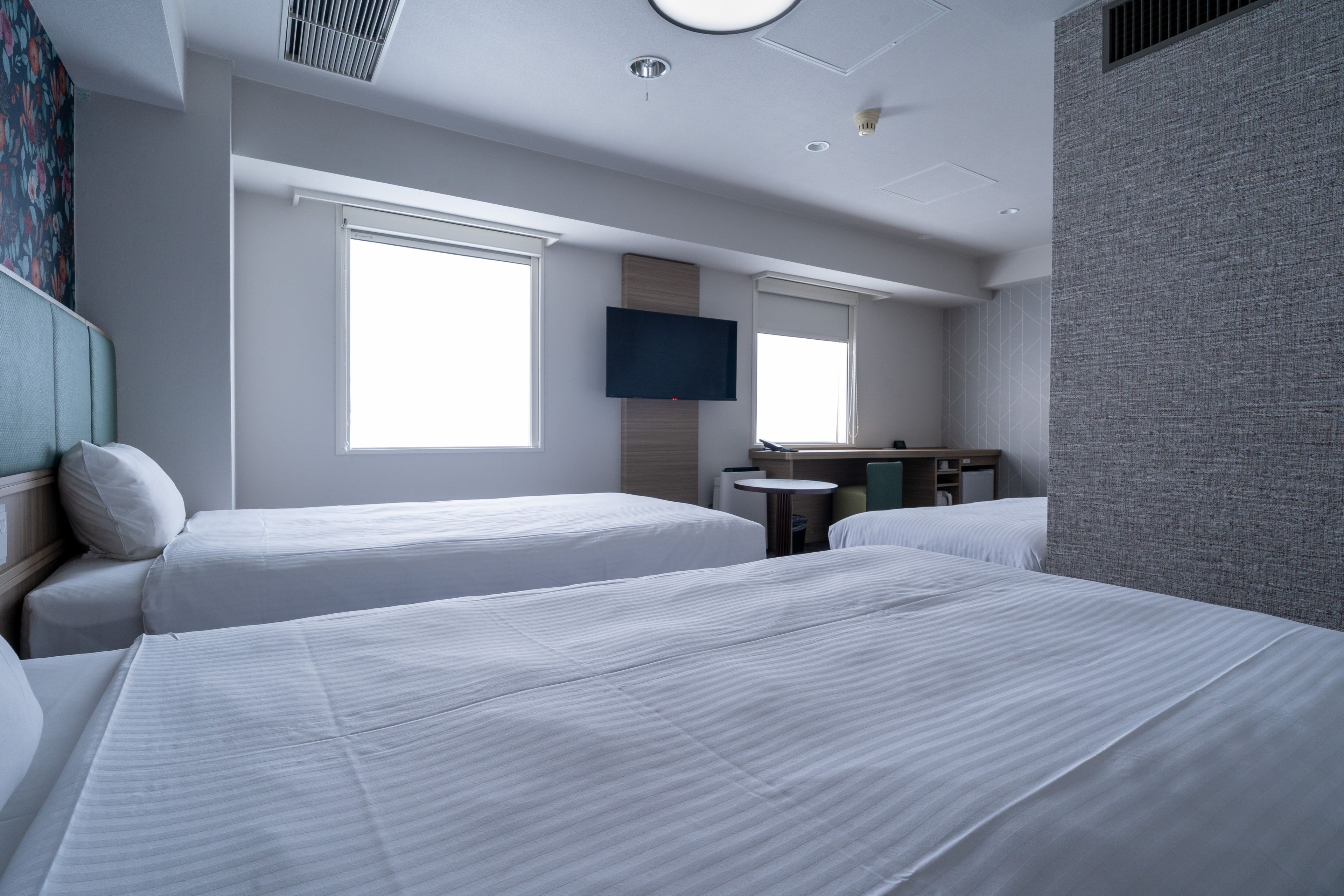 A hotel room with two beds, a desk, a chair, a flat-screen TV mounted on the wall, and a window.