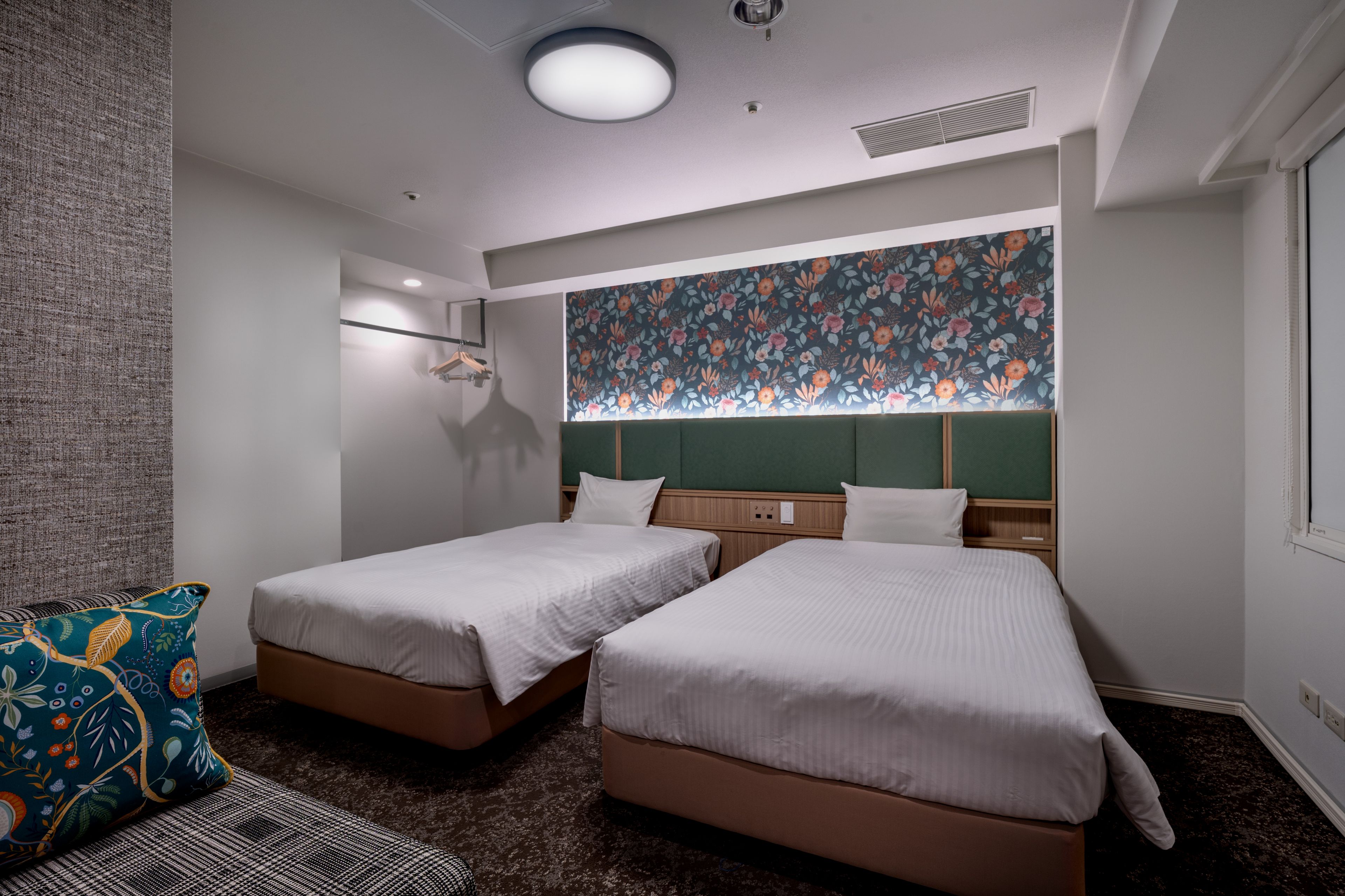 A hotel room with two beds, a patterned wall, a hanging light fixture, and a window.