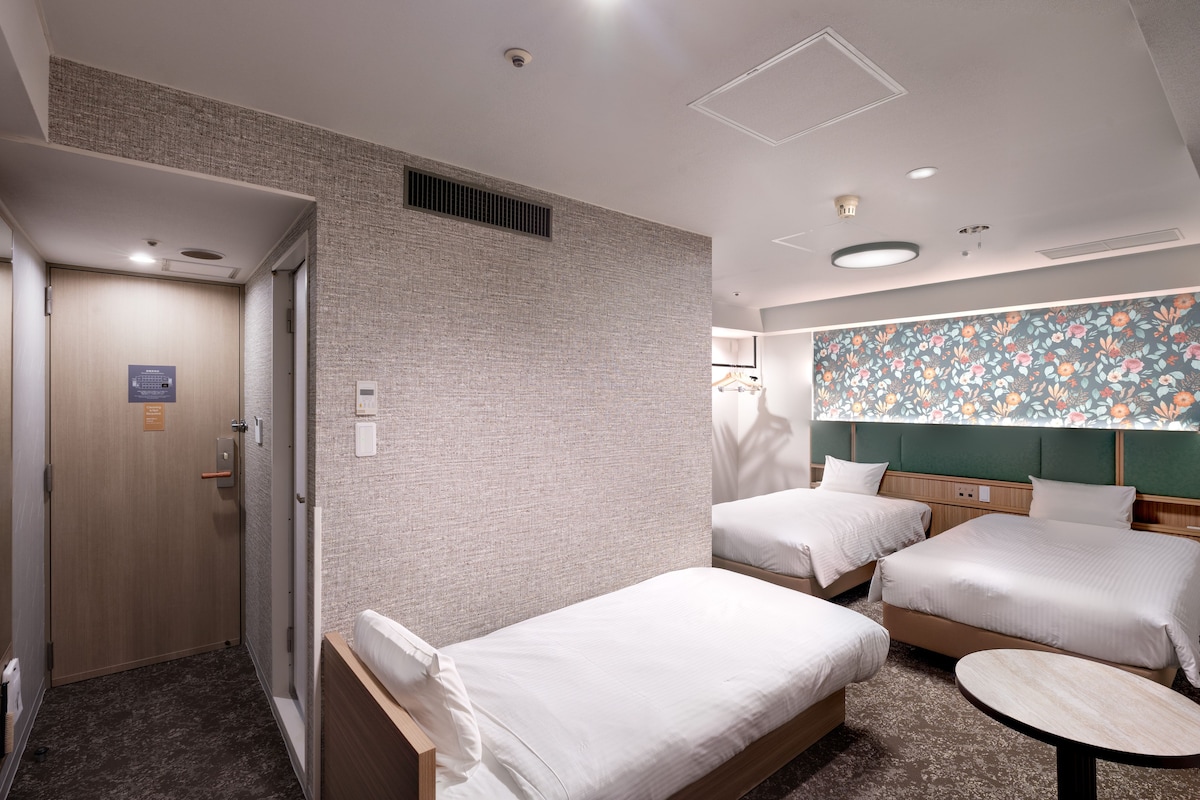 A hotel room with two single beds, a small round table, a shower area, and a bathroom with a towel rack.
