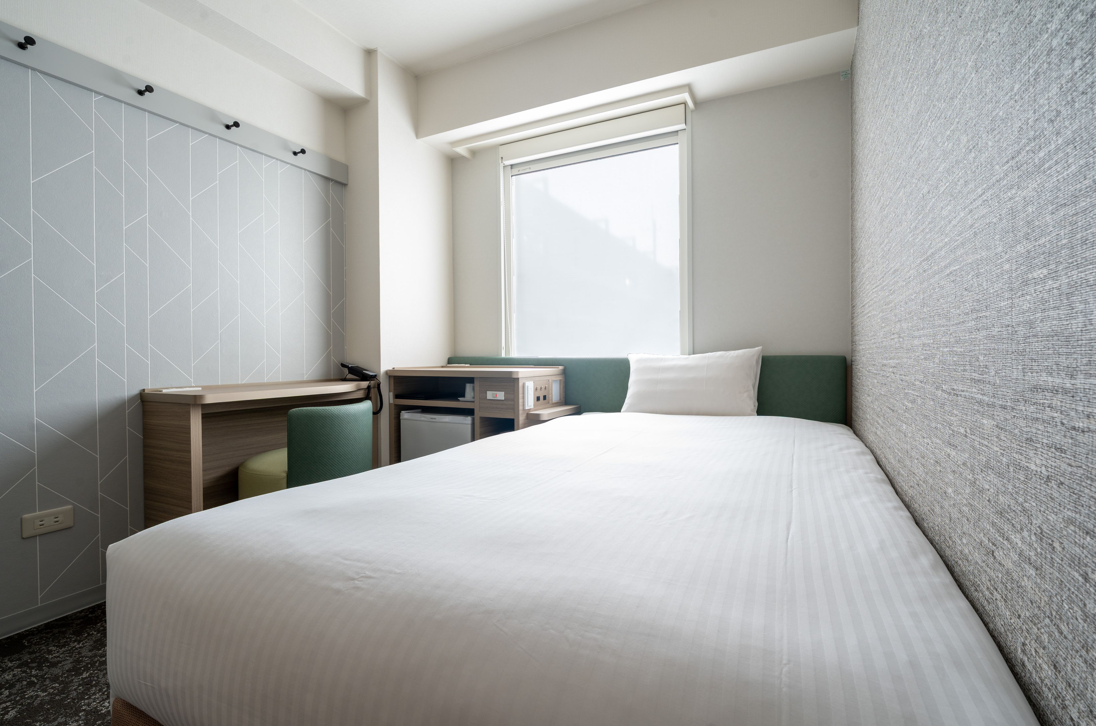 A hotel room with a bed, a desk, a chair, a window, and a wardrobe.