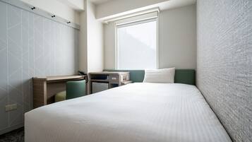 A hotel room with a bed, a desk, a chair, a window, and a wardrobe.
