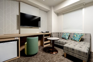 A modern living room with a flat-screen TV, a sofa, a small round table, and a green chair. - HOTEL ARC ONE OmiyaNakaurawa Ekimae (Saitama-shi)