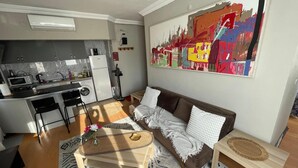 A compact living space with a kitchenette, a sofa, a coffee table, and a painting on the wall. - Cozy 1-bedroom flat in near Old Town with AC and balcony (Antalya)