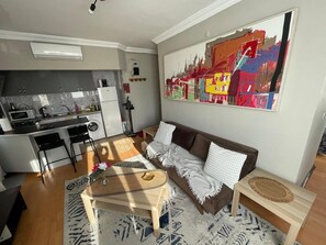 Ein kleiner Wohnbereich mit Küchenzeile, einer Couch, einem Couchtisch und einem Bild an der Wand.
