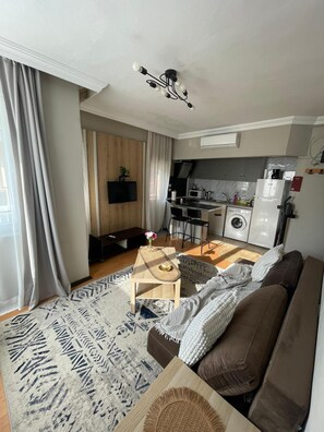 A modern living room with a sofa, coffee table, and a TV mounted on the wall. - Cozy 1-bedroom flat in near Old Town with AC and balcony (Antalya)