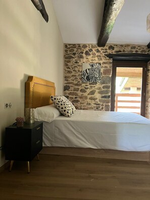 A bedroom with a stone wall, a bed with white bedding, a wooden headboard, a nightstand with a lamp, and a zebra artwork on the wall.
