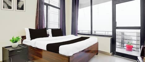 Un dormitorio con cama de madera, una mesita de noche, una planta en maceta y ventanas amplias con cortinas.