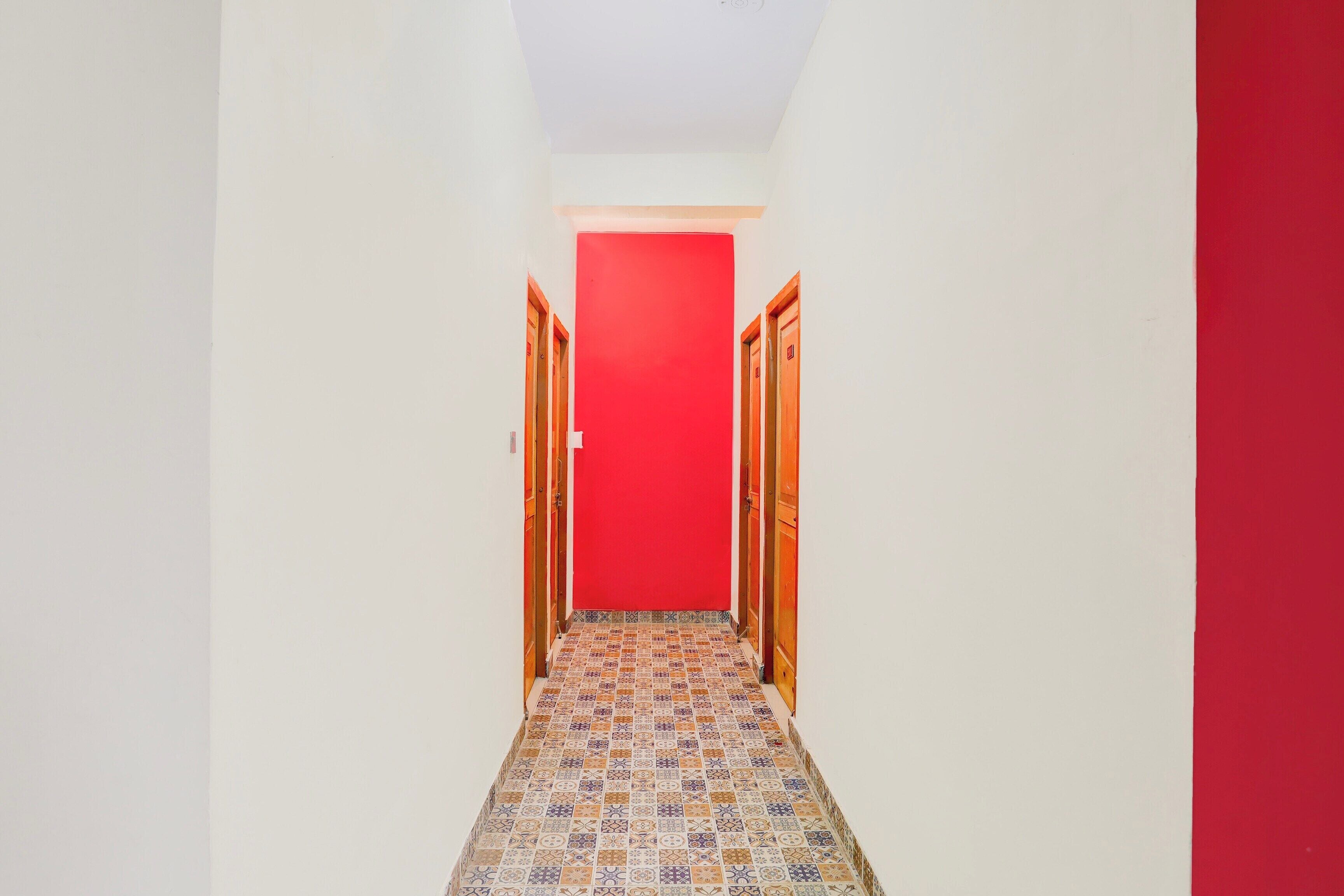 A narrow hallway with patterned floor tiles, white walls, and a red door at the end.