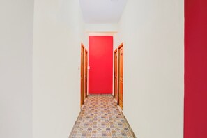 A narrow hallway with patterned floor tiles, white walls, and a red door at the end.
