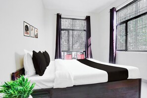 A single bed with white and black bedding, a nightstand, a potted plant, and a window with curtains.