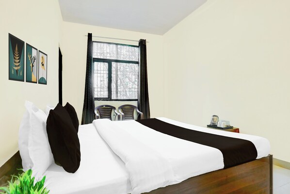 A hotel room with a bed, two chairs, a window with curtains, and artwork on the wall.