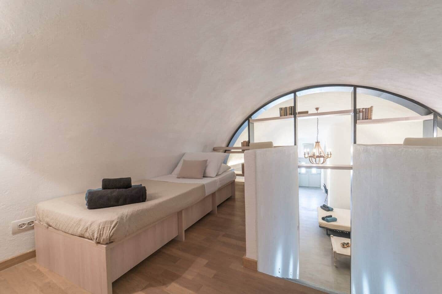 Ein gemütlicher Raum mit gewölbter Decke, einem integrierten Bett und Blick auf eine Küche durch eine Glastrennwand.