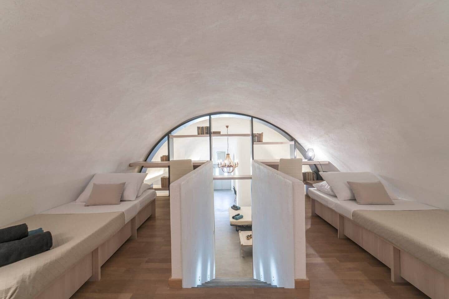 Una habitación acogedora, parcialmente abierta, con dos camas, una mesa central y un candelabro.
