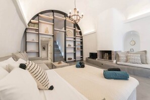 A modern bedroom with a bed, a sofa, a fireplace, and a bookshelf. - Villa LuxL Winery Villa (Mesaria)
