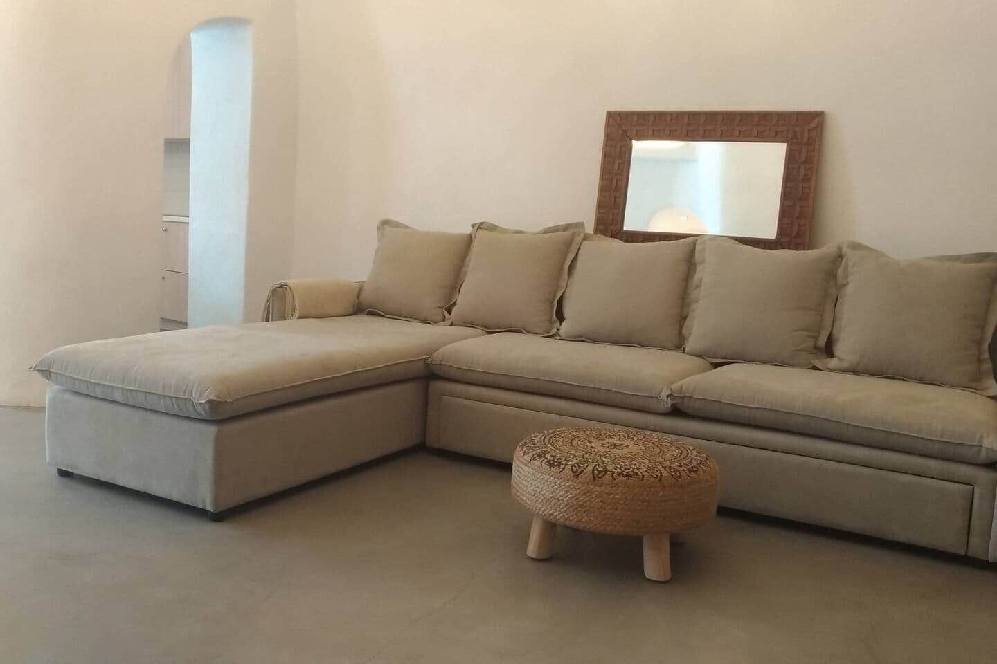 A L-shaped sectional sofa with a matching ottoman, a mirror with a brick frame, and a white wall.