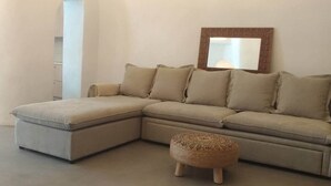 Un sofá seccional en forma de L con un reposapiés a juego, un espejo con marco de ladrillo y una pared blanca.